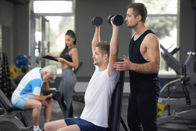 Ajuste perfeito homem malhando na academia com personal trainer. | Foto ...