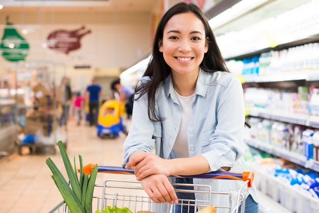 Alegre jovem mulher asiática com carrinho de compras no supermercado Foto gratuita