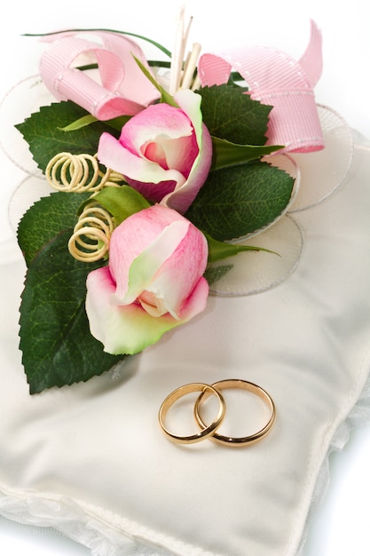 Alianças de casamento de ouro no travesseiro branco com rosa Foto Premium