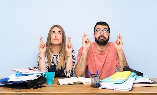 Alunos com muitos livros com os dedos cruzando e desejando o melhor Foto Premium
