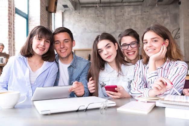 Alunos sentados à mesa com livros e tablet e sorrindo olhando para a câmera Foto gratuita