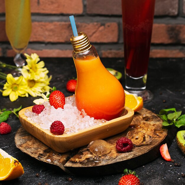 As garrafas de vidro da ampola com suco de frutos tropicais alaranjado fresco na placa com congre cubos e strawbesrries. relaxamento de férias desintoxicação limpeza bem-estar Foto gratuita