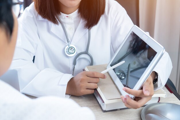 As mãos asiáticas do doutor da mulher usam o estilete que apontam o monitor da tabuleta para explicam ao paciente. Foto Premium