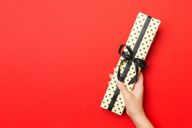 As mãos da fêmea segurando uma caixa de presente listrada com fita colorida sobre fundo vermelho. conceito de natal ou outra caixa de presente artesanal de férias, vista superior do conceito com espaço de cópia Foto Premium