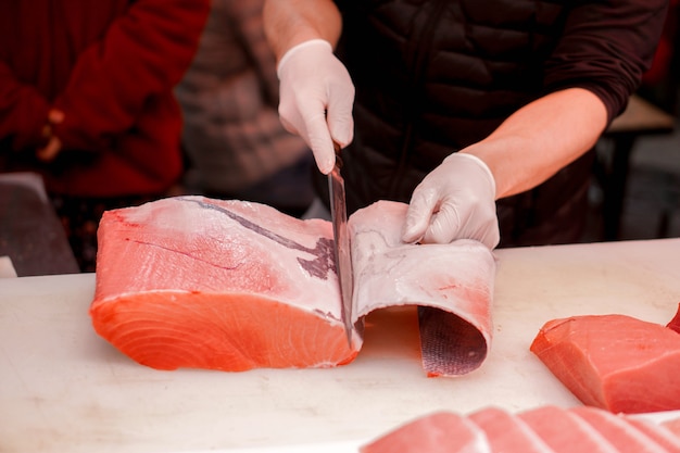 As mãos do cozinheiro chefe japonês que usam a faca do cozinheiro chefe cortaram a parte de peixes de atum frescos para a venda ao cliente no mercado de peixes da manhã, japão. Foto Premium