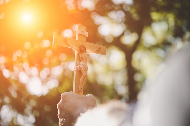 As mãos masculinas segurando jesus de madeira atravessam o céu com o fundo da natureza. Foto gratuita