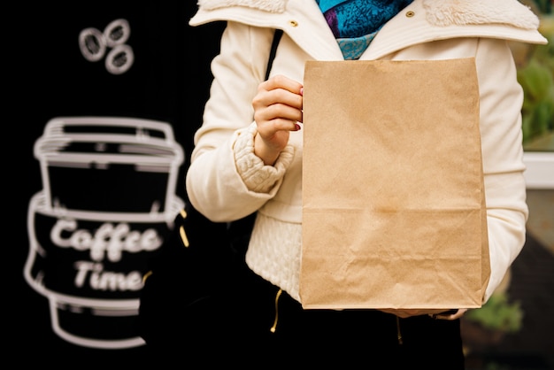 As mãos seguram uma sacola artesanal com comida e um copo de papel com café ou chá. conceito de comida para levar Foto Premium