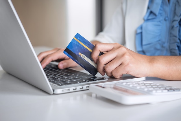 As mãos segurando um cartão de crédito e digitando no laptop para compras on-line e pagamento fazem uma compra Foto Premium