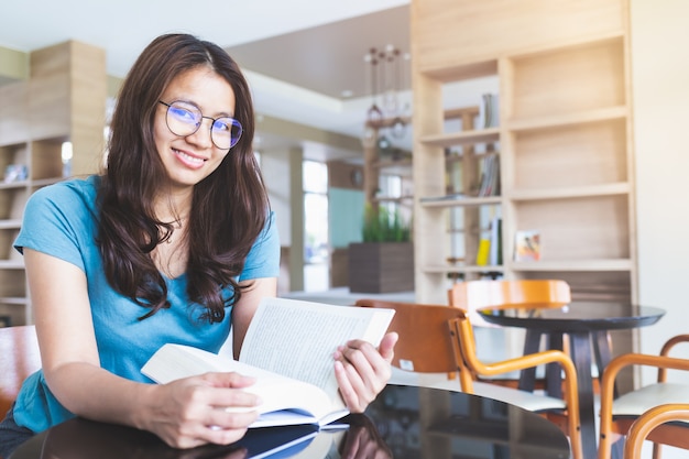 As mulheres asiáticas de óculos estão sorrindo e lendo livros na biblioteca Foto Premium