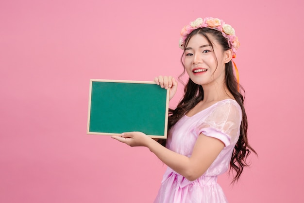As mulheres bonitas, vestidas com vestidos de princesa rosa, prendem uma placa verde em um rosa. Foto gratuita