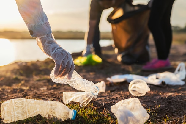 As pessoas voluntárias mantendo a garrafa de plástico de lixo em saco preto no rio park no pôr