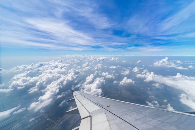 Asa do voo do avião acima das nuvens no fundo do céu azul através da