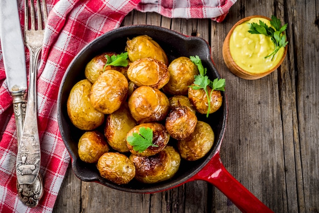Assado na frigideira, batatas jovens inteiras, comida vegetariana caseira, mesa rústica velha de madeira, com molho, cópia espaço Foto Premium