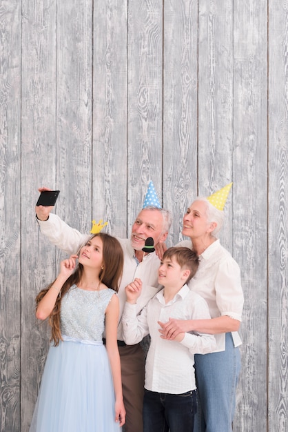 Avô, desgastar, chapéu partido, levando, selfie, ligado, telefone móvel, com, seu, netos, segurando, papel, adereços Foto gratuita