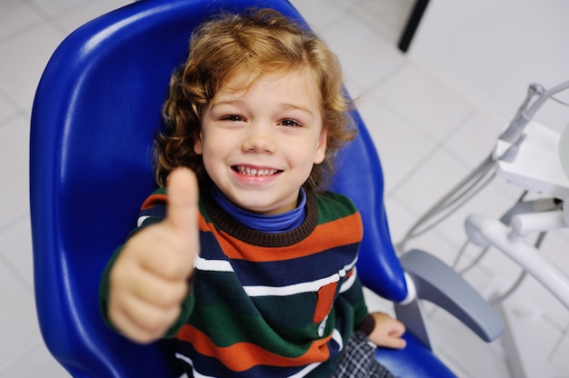 Bebê fofo em um suéter listrado na recepção no dentista com polegares para cima Foto Premium