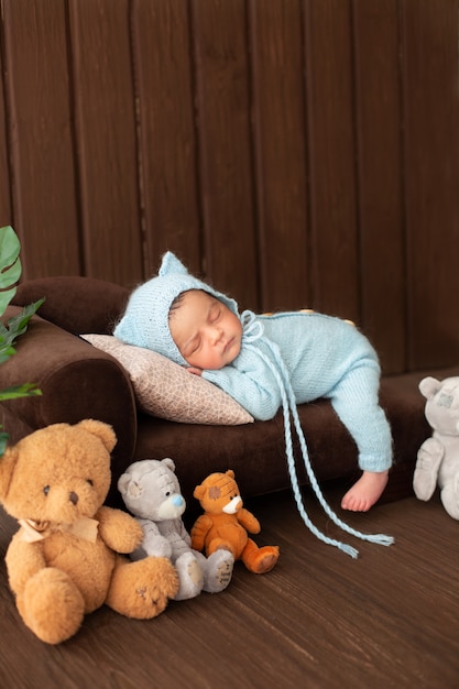 Bebe Menino Recem Nascido Descansando No Sofa Marrom Em Pijama De Malha Azul Rodeado Por Ursos De Brinquedo Bonito Foto Gratis