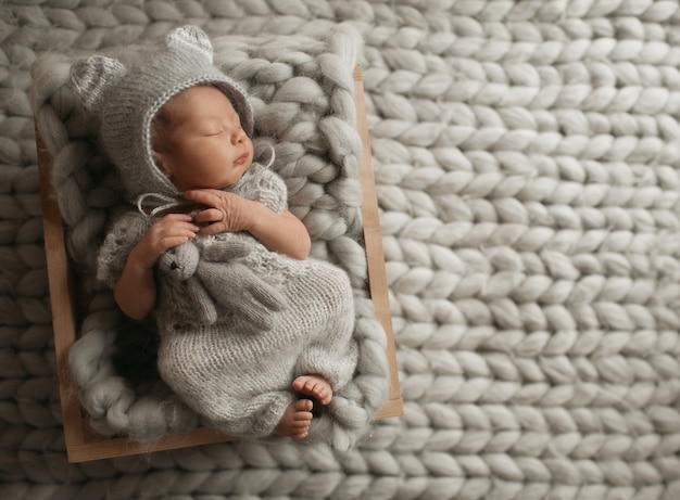 Bebê minúsculo com roupas cinzentas dorme com um cobertor de lã Foto gratuita