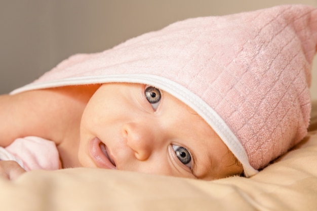 Bebê surpreendido com grandes olhos azuis e boca aberta deitada na barriga sob a toalha rosa após banho Foto Premium
