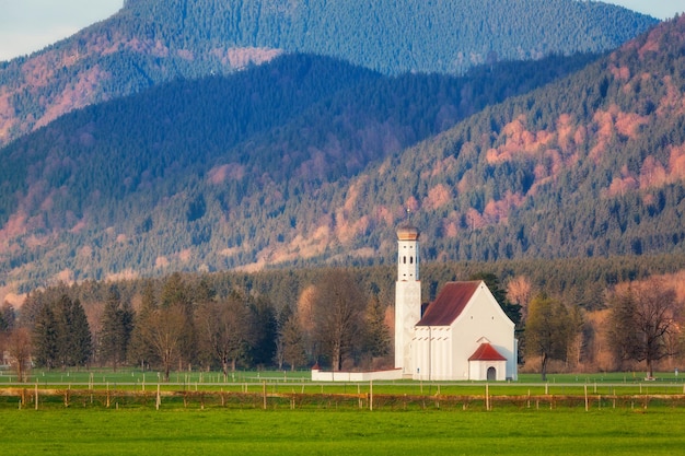 Bela igreja branca no prado verde no fundo de árvores e montanhas na