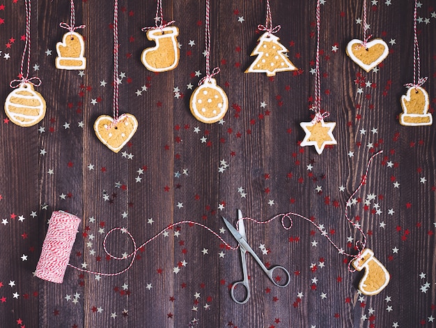 Biscoitos de gengibre na corda para a decoração da árvore de natal com tesoura e fio de ano novo na mesa de madeira Foto gratuita