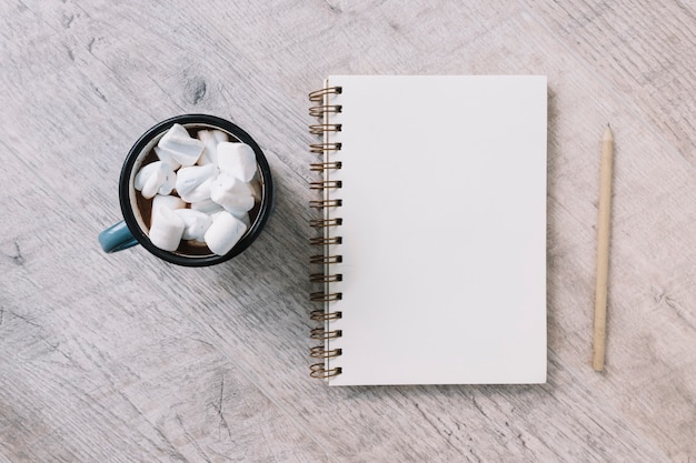 Bloco de notas em branco com copo de marshmallows Foto gratuita