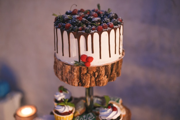 Bolo e cupcakes com frutas em uma prateleira de madeira à luz de velas Foto Premium