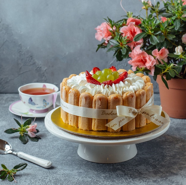 Bolo tiramisu com biscoitos de dedo de senhora e bagas com uma xícara de chá e flores. Foto gratuita