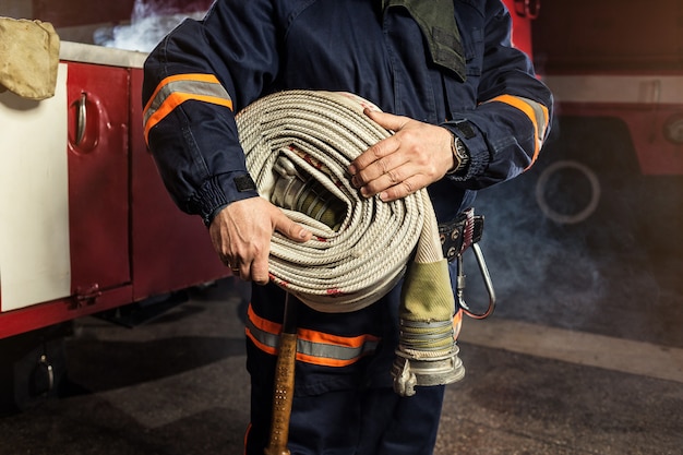 Bombeiro (bombeiro) em ação com uma mangueira de incêndio enrolada perto de  um caminhão de bombeiros. segurança de emergência. proteção, resgate do  perigo. | Foto Premium
