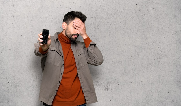Bonito, homem, com, barba, com, perturbado, segurando, quebrada, smartphone, sobre, textured, parede Foto Premium