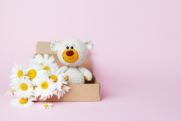 Brinque o urso de peluche em uma caixa do ofício com as margaridas isoladas em um fundo cor-de-rosa. fundo de bebê copie o espaço, vista superior Foto Premium