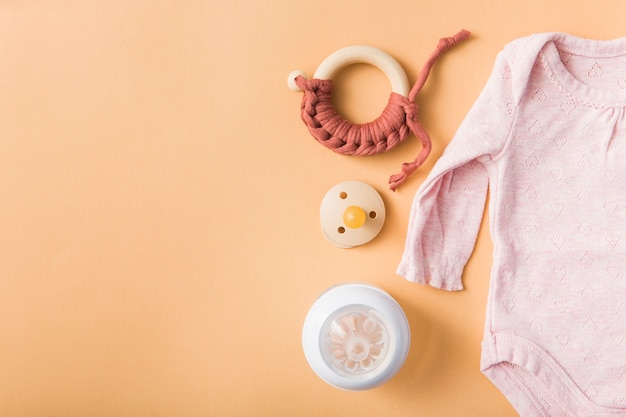 Brinquedo; chupeta; garrafa de leite e rosa bebê onesie sobre um fundo laranja Foto gratuita