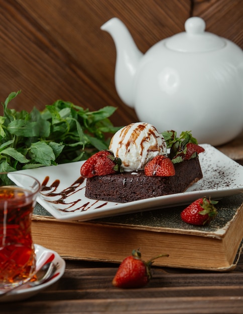 Brownie de chocolate com bola de sorvete e morangos e um copo de chá Foto gratuita