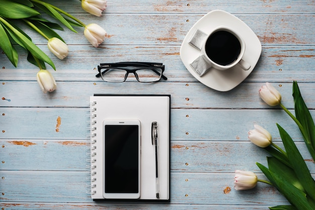 Buquê de tulipas com um caderno vazio, uma xícara de café e um smartphone em um fundo de madeira Foto Premium