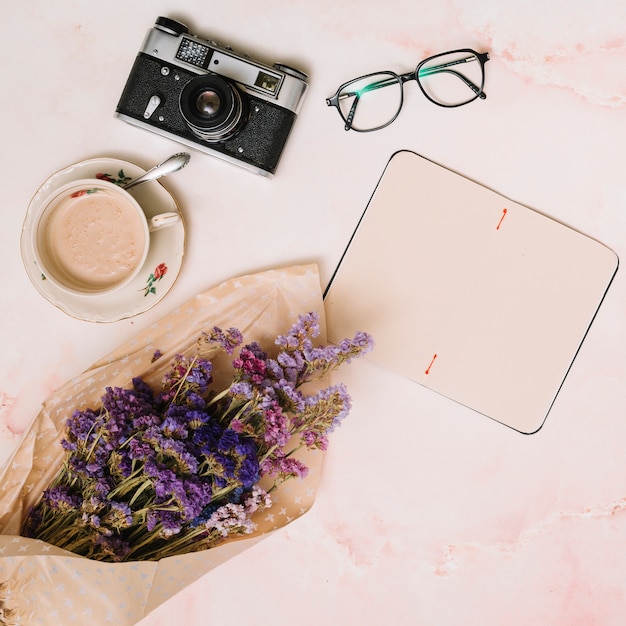 Caderno em branco com uma xícara de café, câmera e óculos na mesa Foto gratuita