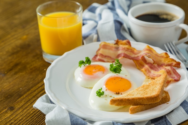 Café da manhã americano com ovos fritos, bacon, torradas, panquecas, café e suco Foto Premium
