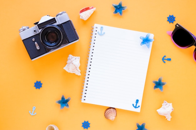 Câmera com óculos escuros, conchas e caderno em branco Foto gratuita