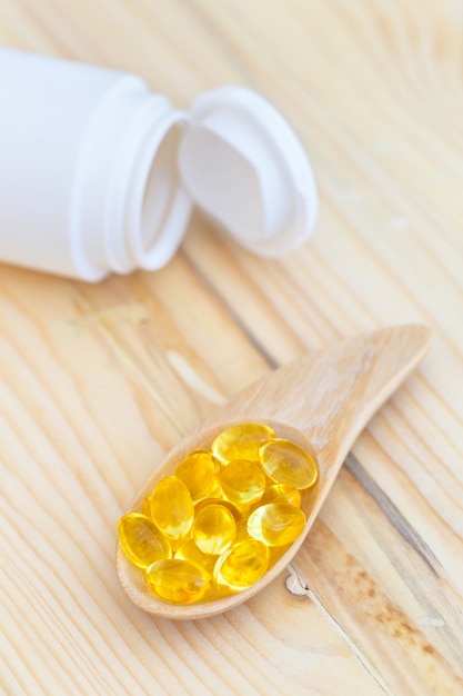 Cápsulas de óleo de peixe com ômega 3 e vitamina d na madeira colher com uma garrafa na textura de madeira Foto Premium