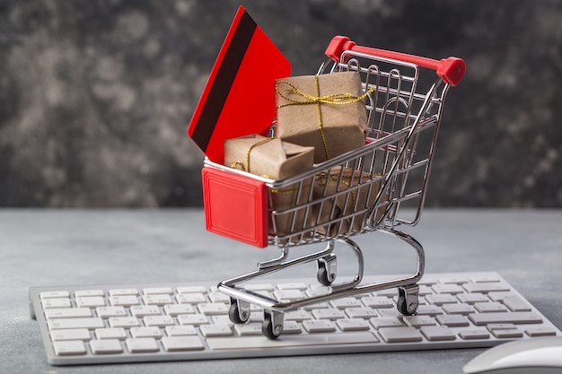 Carrinho de compras pequeno com presentes e cartão de crédito em um teclado de laptop Foto Premium