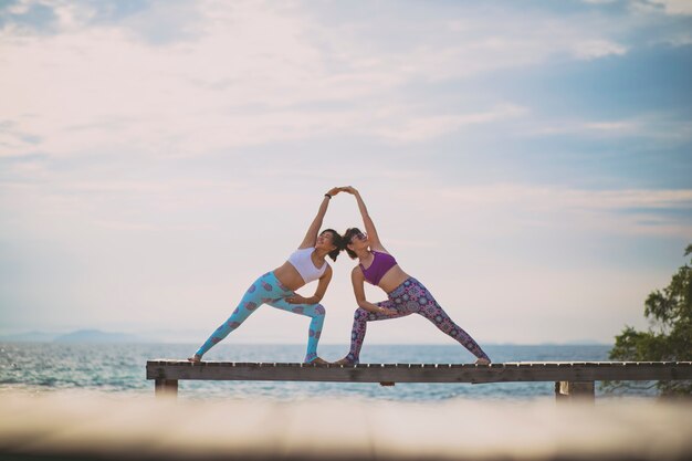 Casais de mulher jogando pose de ioga no cais da praia com a luz do sol Foto Premium