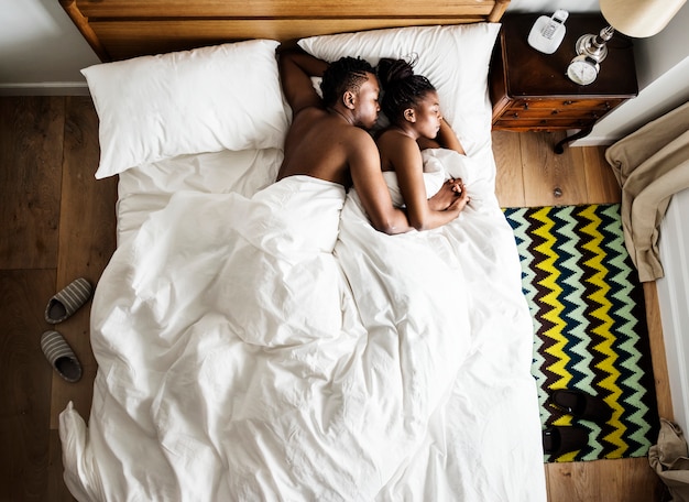 Casal de ascendência africana dormindo na cama aconchegando se e abraçando Foto Premium