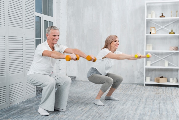 Casal mais velho sorridente, realizando exercícios com halteres em casa Foto gratuita