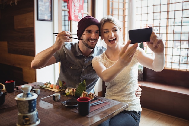 Casal tomando selfie enquanto come sushi Foto gratuita aquitemtrabalho.com.br