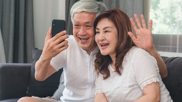 Chamada de vídeo dos pares sênior asiáticos em casa. avós chinesas sênior asiáticas, usando a chamada de vídeo do telefone móvel que fala com as crianças do neto da família ao encontrar-se no sofá no conceito da sala de visitas em casa. Foto gratuita