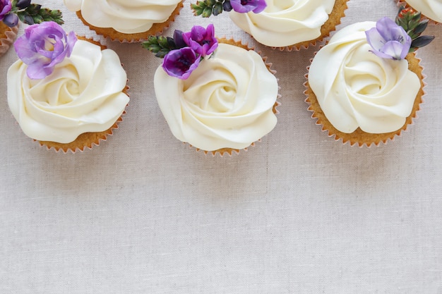 Chantilly glacê cupcakes de baunilha com flores roxas comestíveis Foto Premium