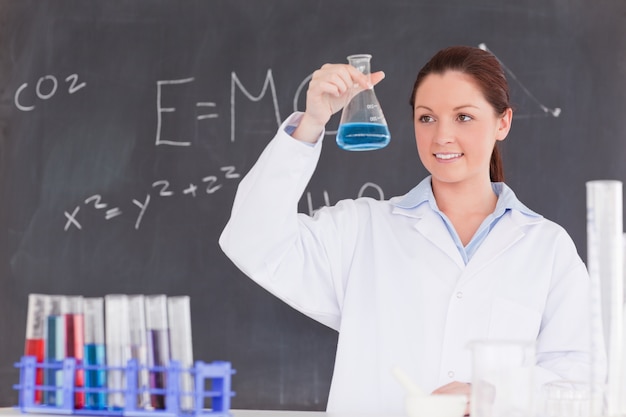 Cientista bonito que olha um recipiente encheu com um líquido azul Foto Premium