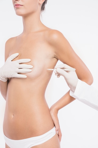 Cirurgião plástico com bisturi perto do peito de mulher Foto gratuita