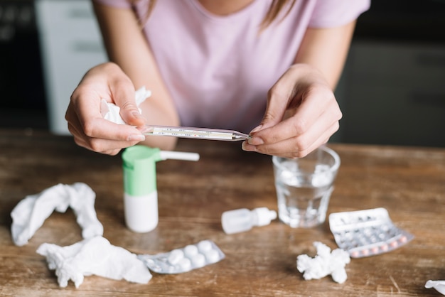 Close-up, de, um, mão mulher, verificar, temperatura, ligado, termômetro, com, medicamentos, ligado, escrivaninha madeira Foto gratuita