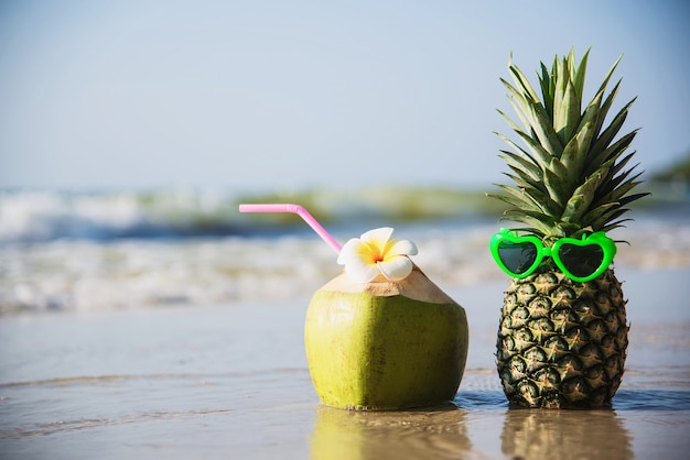 Coco fresco e abacaxi colocar óculos adorável sol na praia de areia limpa com a onda do mar - fruta fresca com conceito de férias sol mar areia Foto gratuita