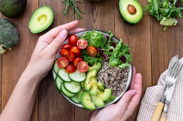 Comida saudável. a mão da mulher segurando a tigela de budha com quinoa, abacate, pepino, salada, tomate, azeite de oliva. Foto Premium