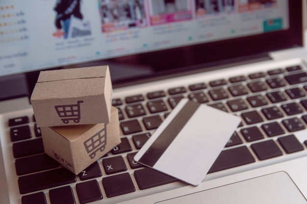Compras on-line conceito - serviço de compras na web on-line. com pagamento por cartão de crédito e oferece entrega em domicílio. pacote ou caixas de papel com um logotipo de carrinho de compras em um teclado de laptop Foto Premium